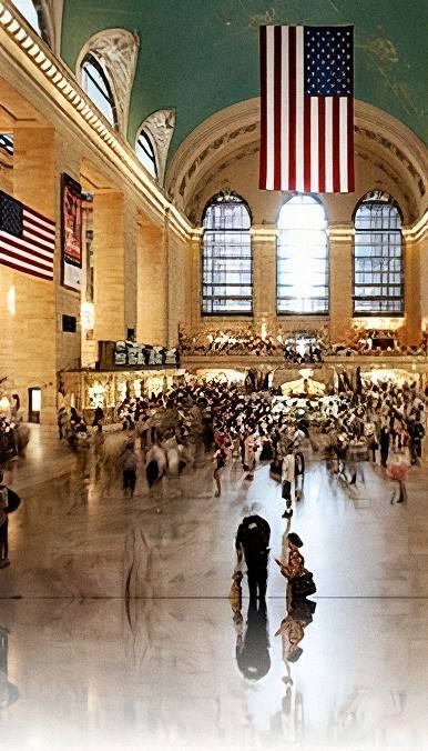 Main concourse of Grand Central Terminal with a large American flag and travelers crossing the floor